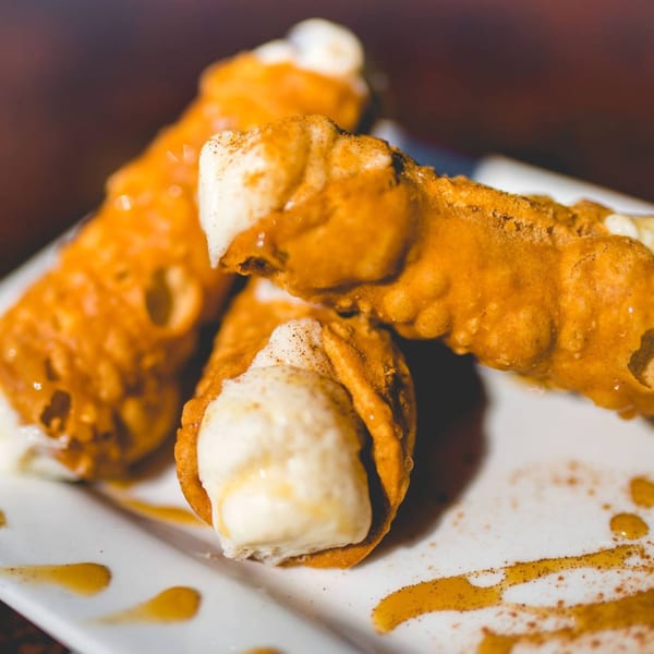 Three golden-brown cannoli filled with white cream, drizzled with honey and cinnamon on a white plate.