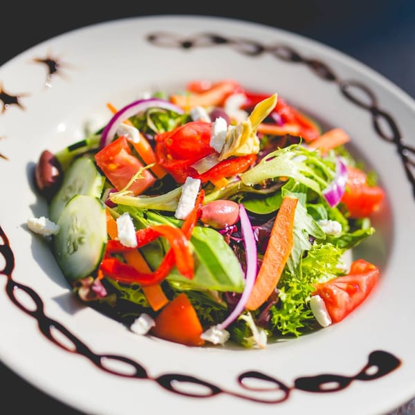 A vibrant Italia Express house salad with mixed greens, tomatoes, cucumbers, red onion, and feta cheese.